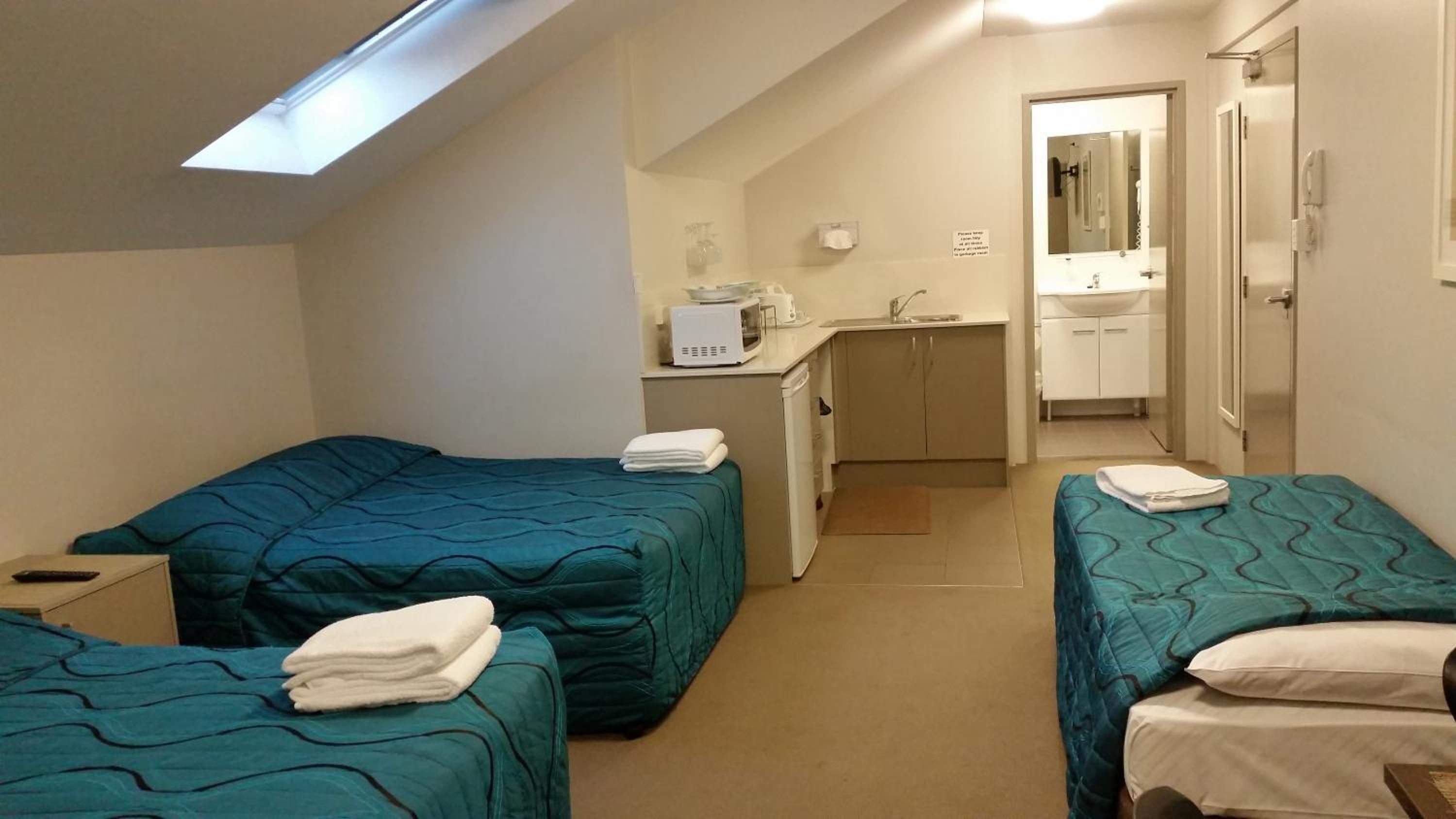 A room with two beds, a kitchenette, a bathroom, and a skylight.