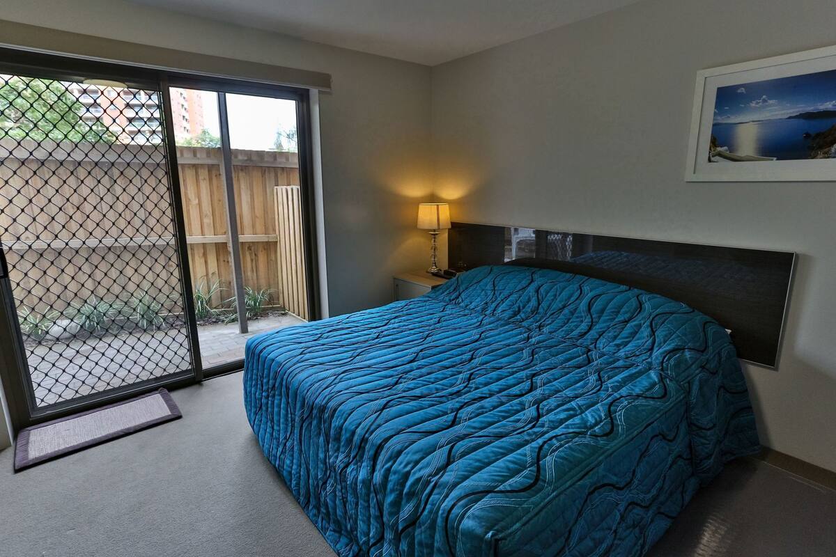 A bedroom with a bed, a nightstand, a lamp, a sliding glass door, and a framed picture on the wall.