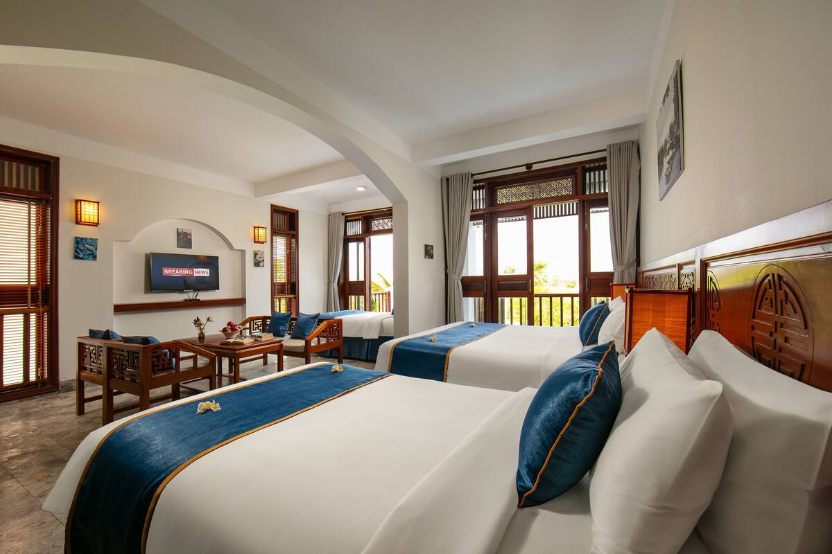 Ein Hotelzimmer mit zwei Betten, einem Fernseher, einem Schreibtisch und einem Balkon.