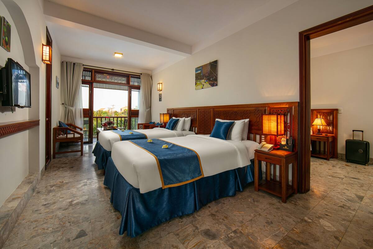 Ein Hotelzimmer mit zwei Betten, einem Schreibtisch, einem Stuhl, einem Fernseher und Blick ins Freie.
