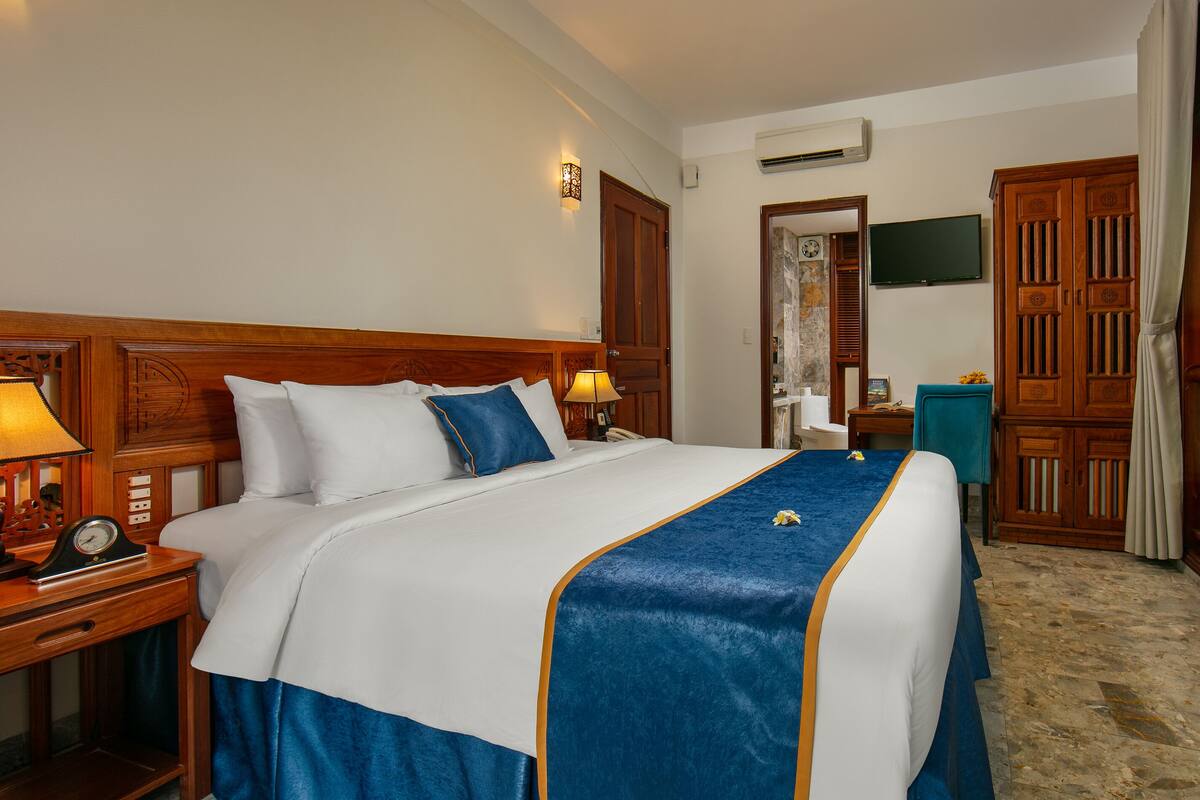 Ein Hotelzimmer mit einem großen Bett, einem Holzkopfteil, Nachttischlampen, einer Uhr und einem an der Wand befestigten Fernseher.