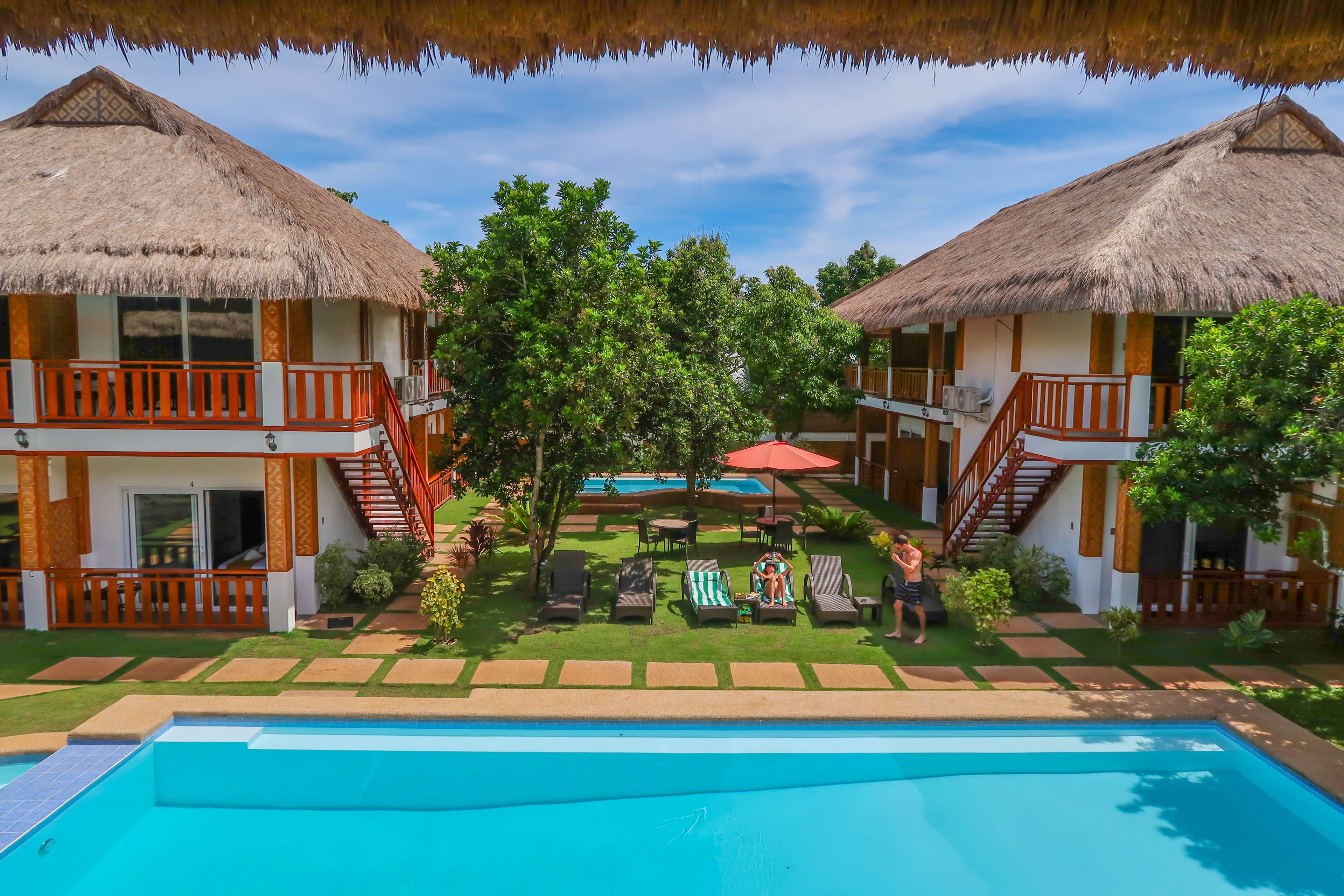 A resort with two thatched-roof buildings, a swimming pool, and outdoor seating areas.