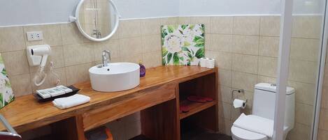 A bathroom with a wooden vanity, a round mirror, a white sink, a toilet, and a trash bin.