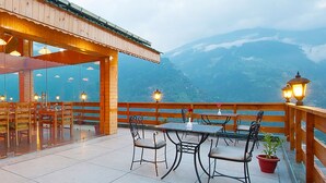 A restaurant with wooden tables and chairs, large windows, and a view of mountains. - Vivaan The Sunrise Resort (Manali)
