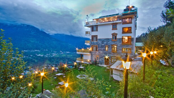A multi-story building with a stone facade, multiple windows, and a balcony with string lights. - Vivaan The Sunrise Resort (Manali)
