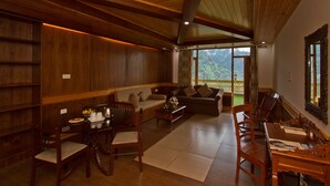 A spacious living area with wooden furniture, a dining table, and a view of mountains through large windows. - Vivaan The Sunrise Resort (Manali)