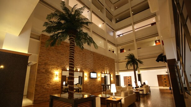 A spacious lobby with a high ceiling, stone walls, and a central palm tree. There are seating areas with tables and lamps. - Hotel Moti Mahal (Mangaluru)
