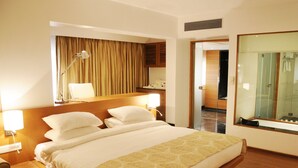 A hotel room with a large bed, bedside lamps, a mirror, and a view of the bathroom. - Hotel Moti Mahal (Mangaluru)