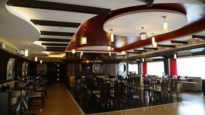 A spacious restaurant with high ceilings, modern lighting fixtures, and a variety of seating arrangements. - Hotel Moti Mahal (Mangaluru)