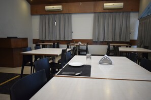 A dining area with tables and chairs, air conditioning units, and curtains. - Hotel The Nook (Madurai)