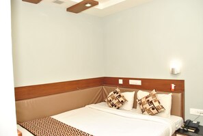A hotel room with a bed, a bedside table, a nightstand, and a wall-mounted light. - Hotel The Nook (Madurai)