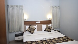 A hotel room with a bed, nightstand, and a wall-mounted light fixture. - Hotel The Nook (Madurai)