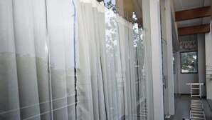 A room with a large window covered by sheer curtains, a ladder, and a visible door. - Hotel The Nook (Madurai)