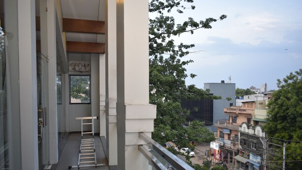 A narrow balcony with a metal ladder, overlooking a street with buildings and trees. - Hotel The Nook (Madurai)