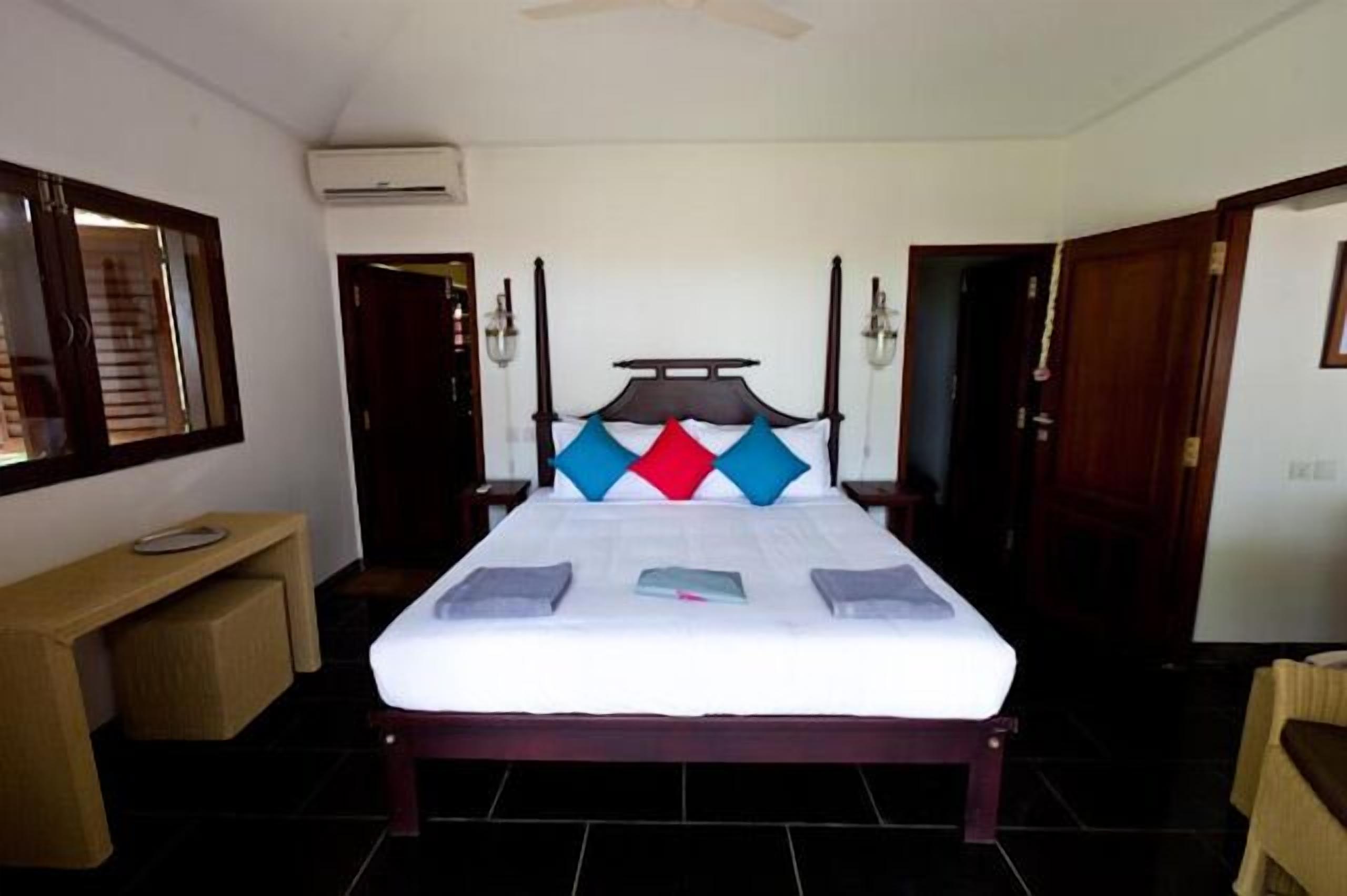 A bedroom with a four-poster bed, a bedside table, a mirror, and a door.