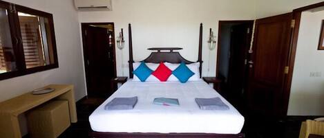 A bedroom with a four-poster bed, a bedside table, a mirror, and a door.