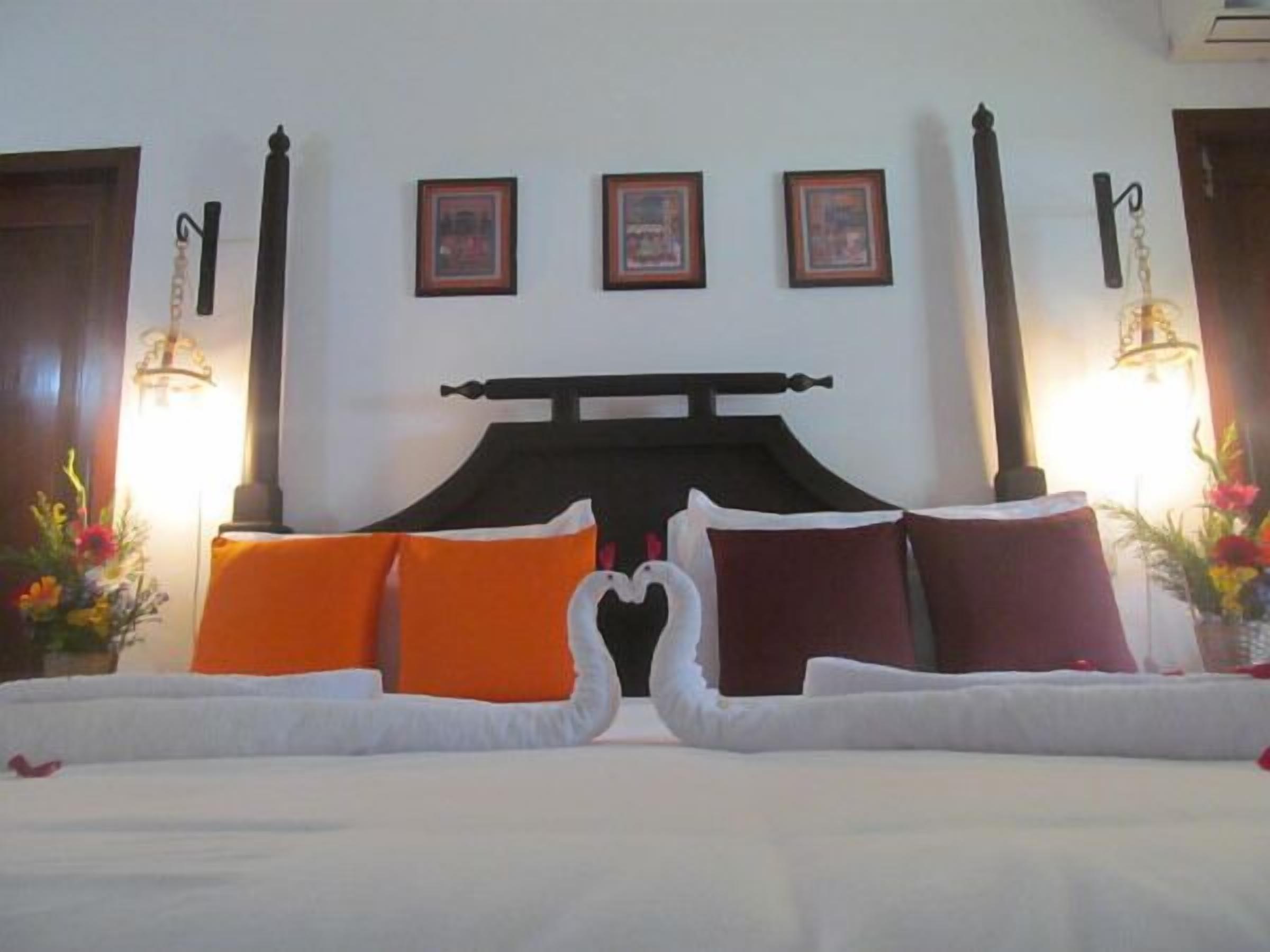A neatly made bed with a white and orange color scheme, a decorative swan headboard, and framed pictures on the wall.