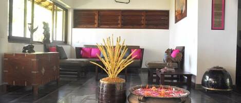 Una habitación con un ventanal grande, techo de madera, un sofá con cojines, un jarrón decorativo y un quemador de incienso tradicional.