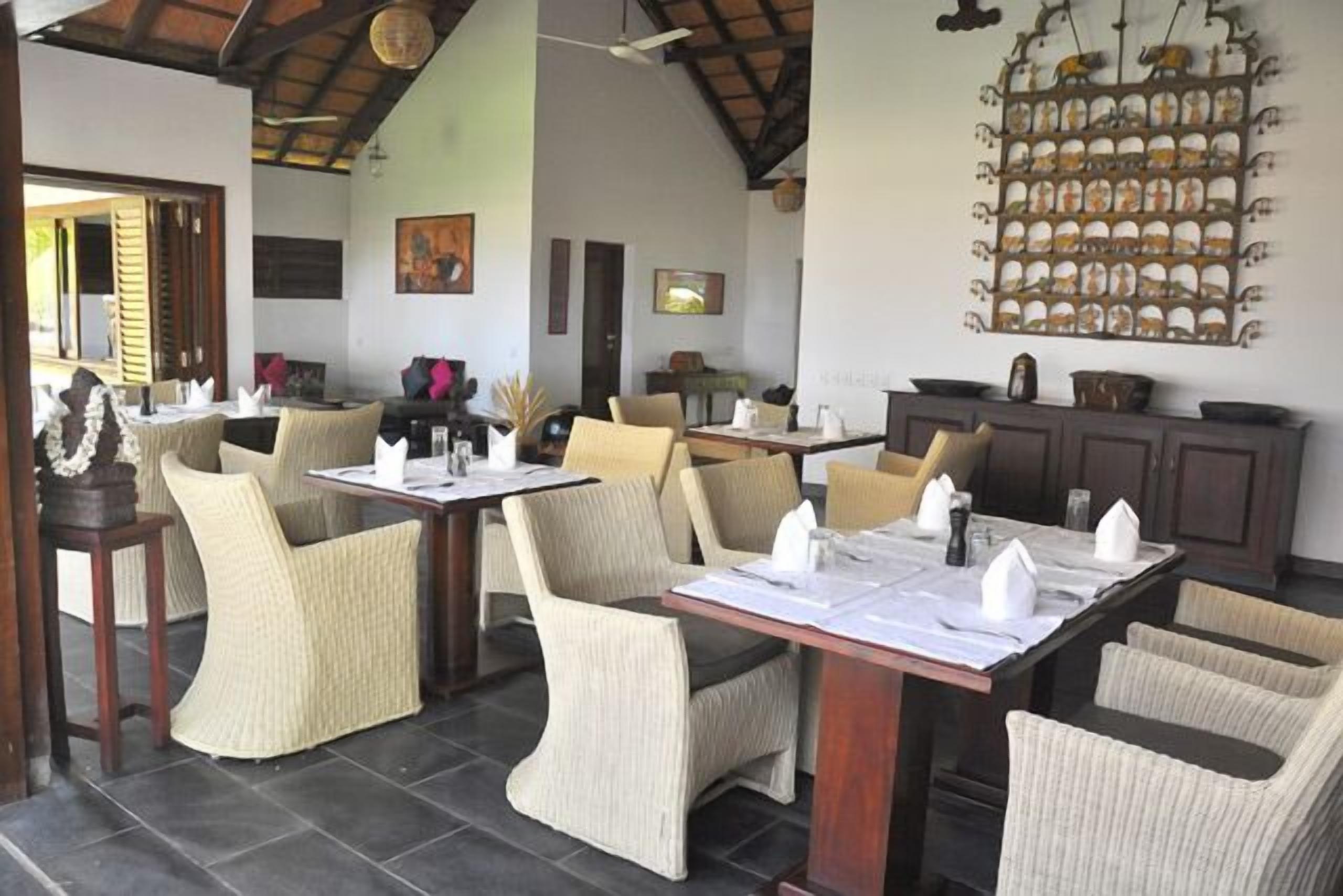 A dining area with wicker chairs and tables, a ceiling fan, and a wall-mounted decorative item.