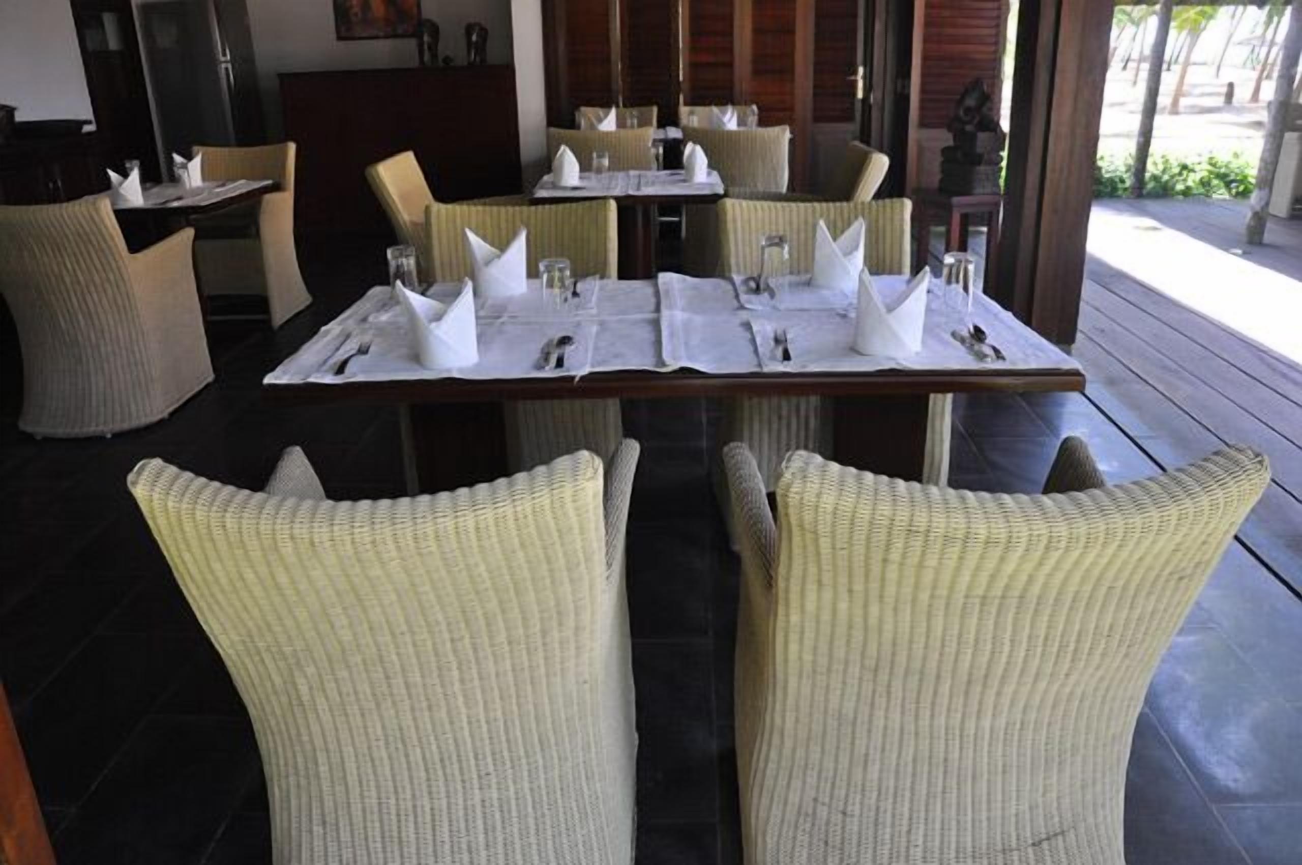A dining area with tables set for two, featuring white tablecloths and neatly arranged cutlery.