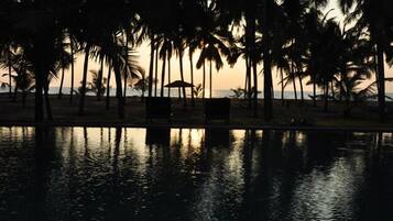 A serene beachfront scene with palm trees and a calm pool reflecting the sunset.