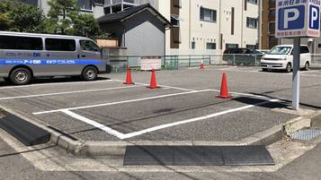 Un parking avec des places délimitées, un fourgon blanc et un bâtiment avec une enseigne.