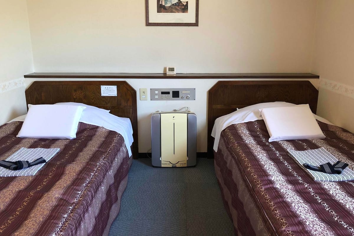 A hotel room with two beds, a bedside table, a clock, and a picture on the wall.