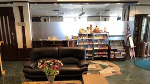 A lobby with a leather sofa, a glass coffee table with a vase of flowers, a wooden side table, a magazine rack, and a display cabinet. - Terminal Art Inn (Niigata)