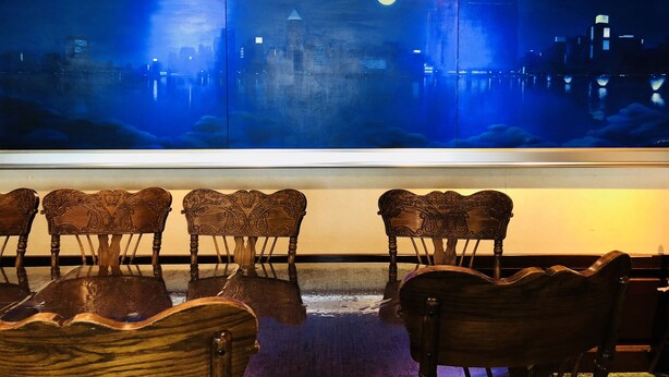 A room with a large cityscape painting, wooden chairs, and a reflective floor. - Terminal Art Inn (Niigata)