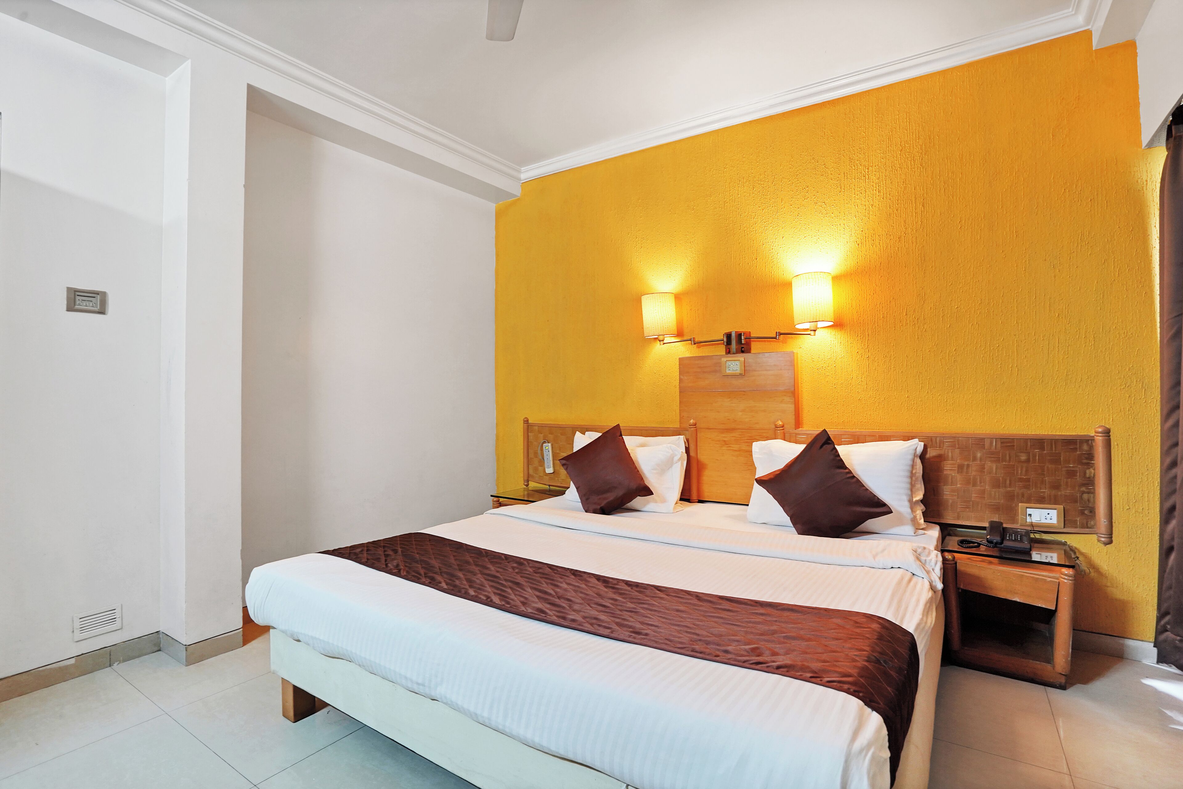 A hotel room with a large bed, two bedside tables, a wooden headboard, and a wall-mounted light fixture.
