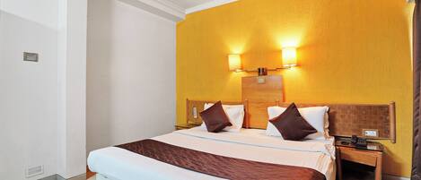 A hotel room with a large bed, two bedside tables, a wooden headboard, and a wall-mounted light fixture.