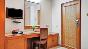 A hotel bathroom with a wooden vanity, a mirror, a television mounted above the counter, and a shower with a glass door. - Hotel Orchard Pune (Pune)