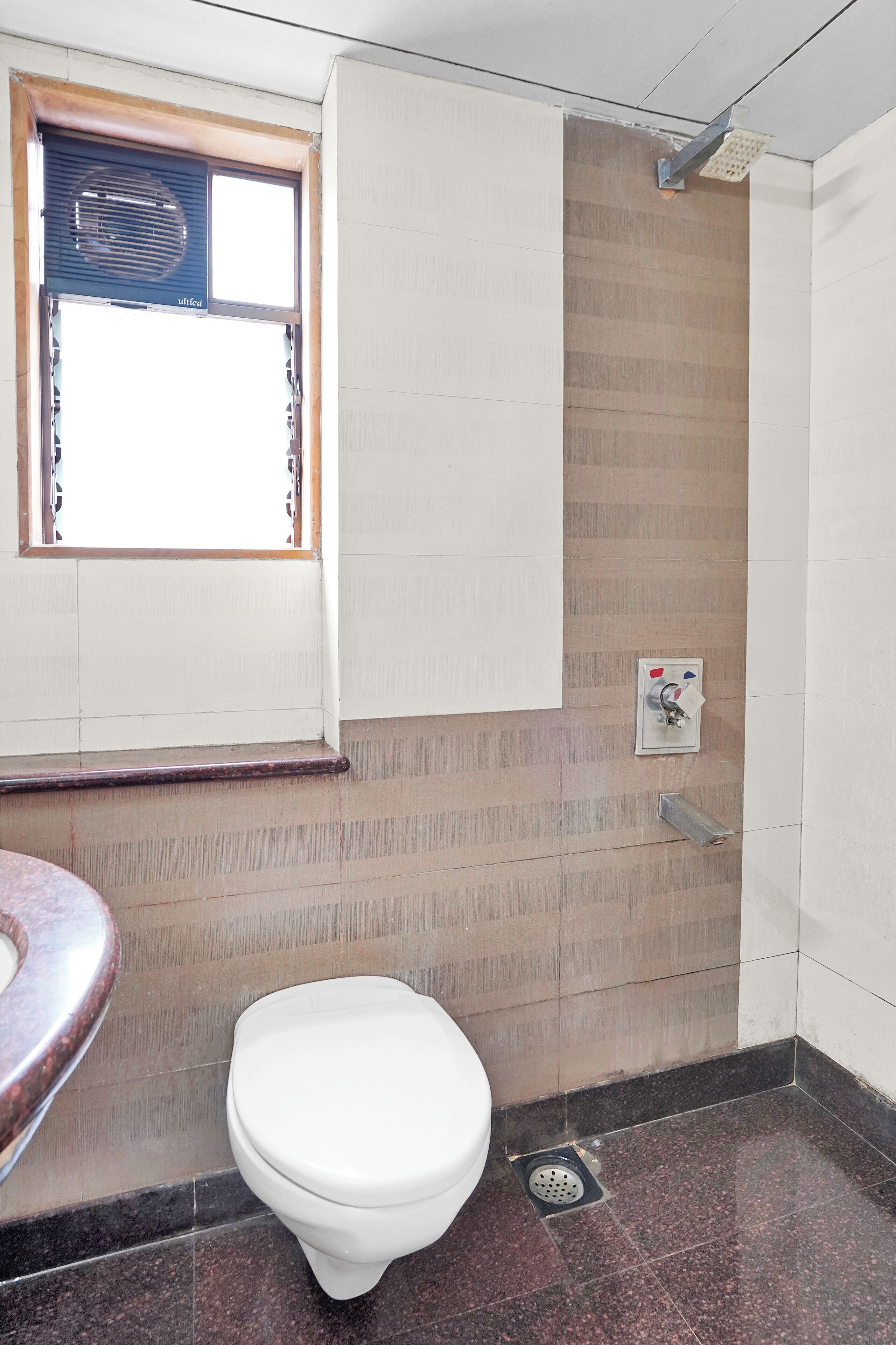 Un baño con inodoro, ventana con persianas, toallero y zona de ducha.