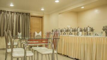 Un comedor con una mesa de vidrio rodeada de sillas de metal, una mesa de buffet con recipientes de comida, y una puerta de madera.