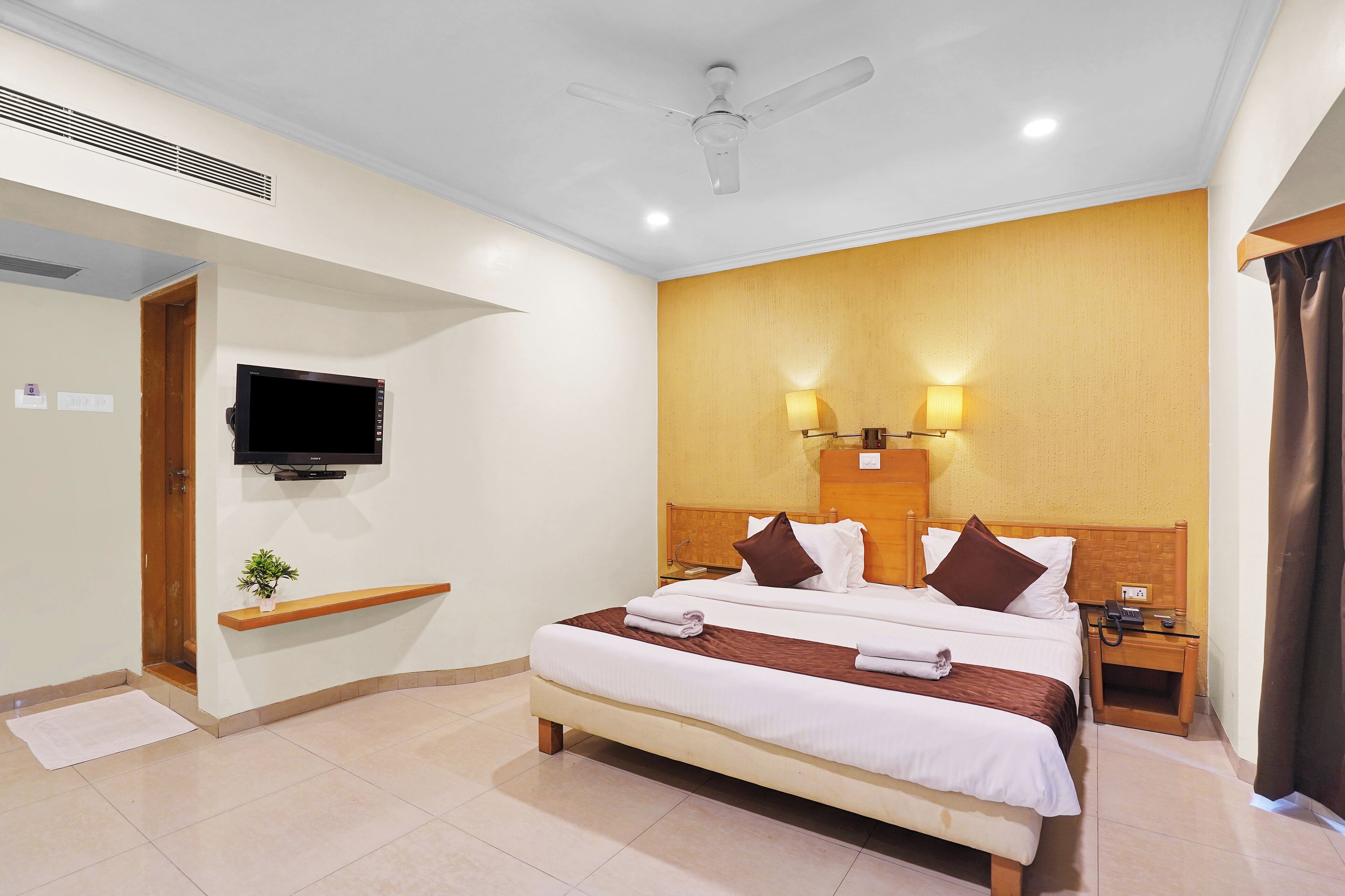 A hotel room with a bed, a TV mounted on the wall, a bedside table, and a nightstand.