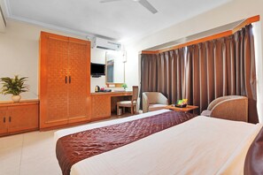 Quarto de hotel com uma cama grande, uma escrivaninha com cadeira, um guarda-roupa e uma televisão.