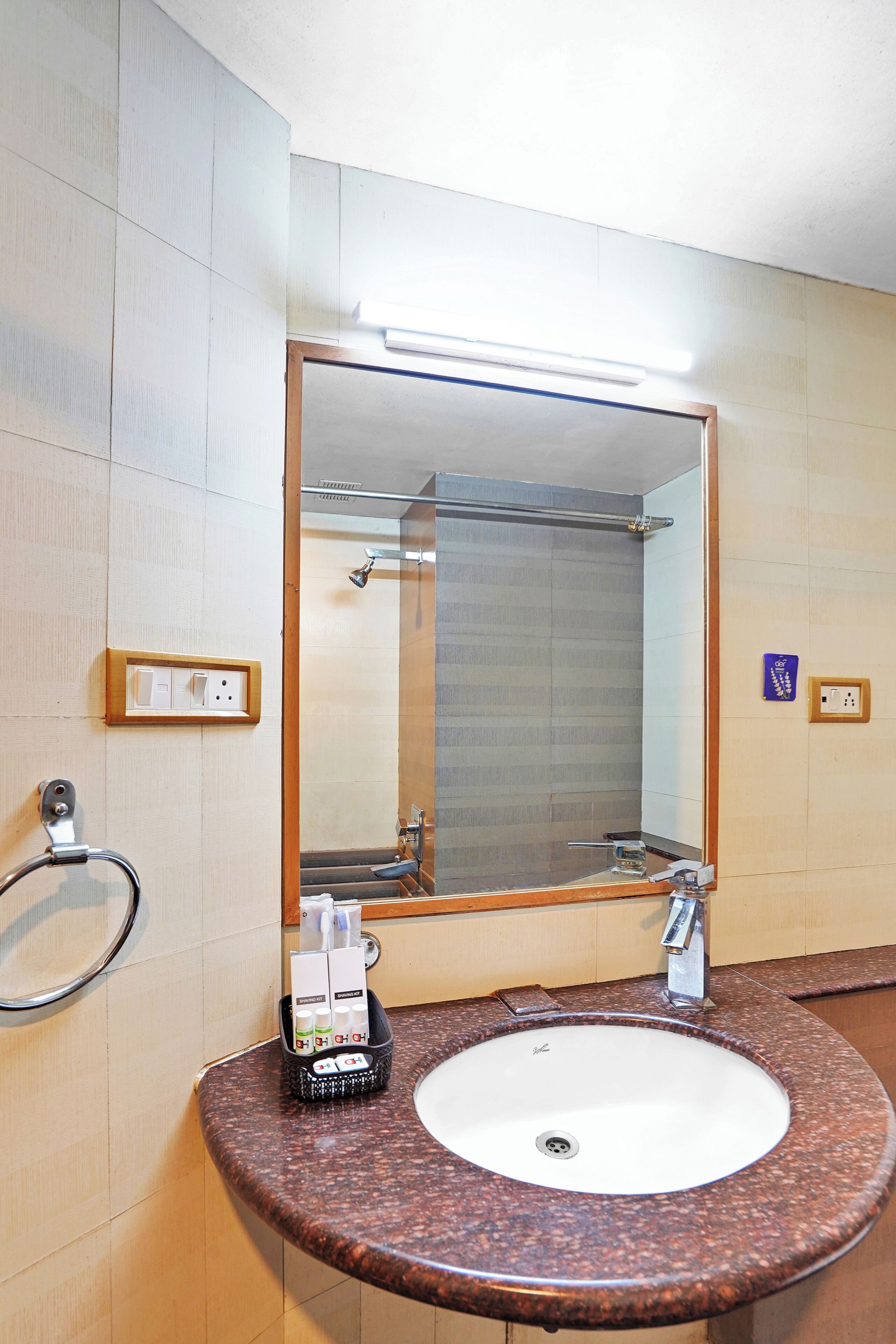 Un baño con lavamanos de granito, un espejo, un perchero y una ducha visible al fondo.