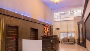 A reception area with a reception desk, a sofa, and a decorative wall piece. - Hotel Orchard Pune (Pune)