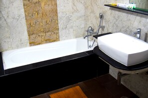 A bathroom with a white bathtub, black countertop, and a marble wall. - Saibala Grand Hotel (Chennai)