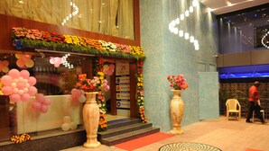 A hotel entrance with a flower-adorned facade, a staircase leading to the entrance, and a reception area with a chair and a person in the background.