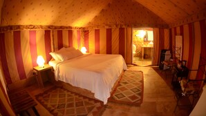 Ein Zeltraum mit Bett, Nachttischlampen, einem gemusterten Teppich und einem kleinen Tisch mit Stühlen.