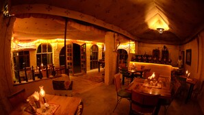 Ein gemütlich beleuchteter Essbereich mit Tischen und Stühlen, eine Bar und eine Aussicht nach draußen durch große Fenster.