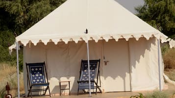 A tent with two lounge chairs and a small table, surrounded by greenery.