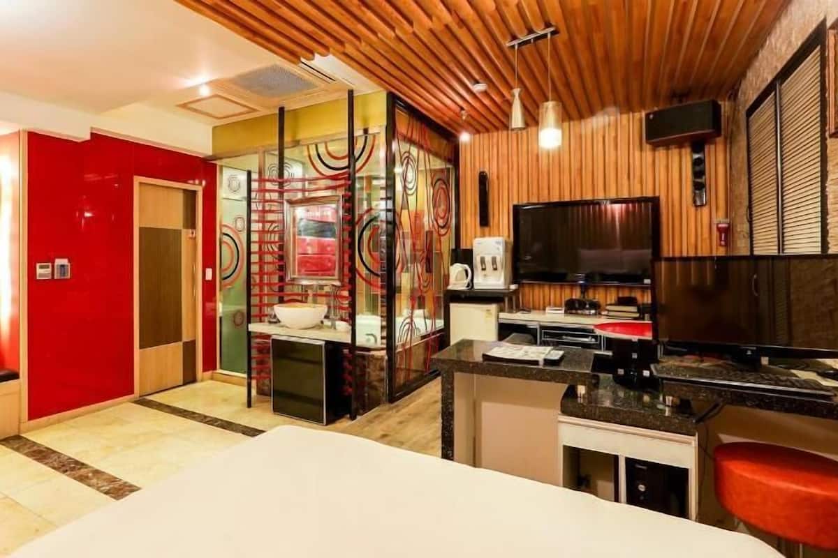 Quarto de hotel moderno com teto de madeira, uma TV, uma escrivaninha e uma parede de destaque vermelha.