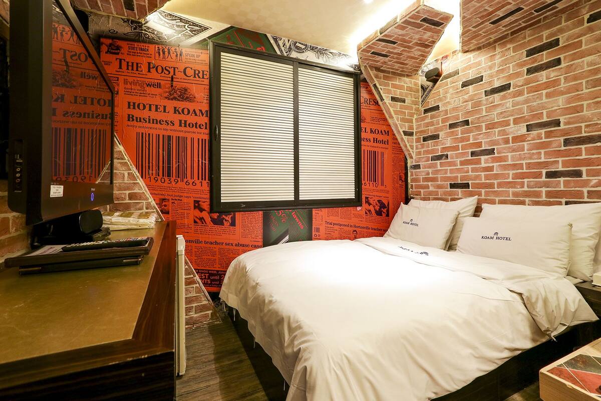 Quarto de hotel com parede de tijolos, cama com roupa de cama branca e janela com persianas.