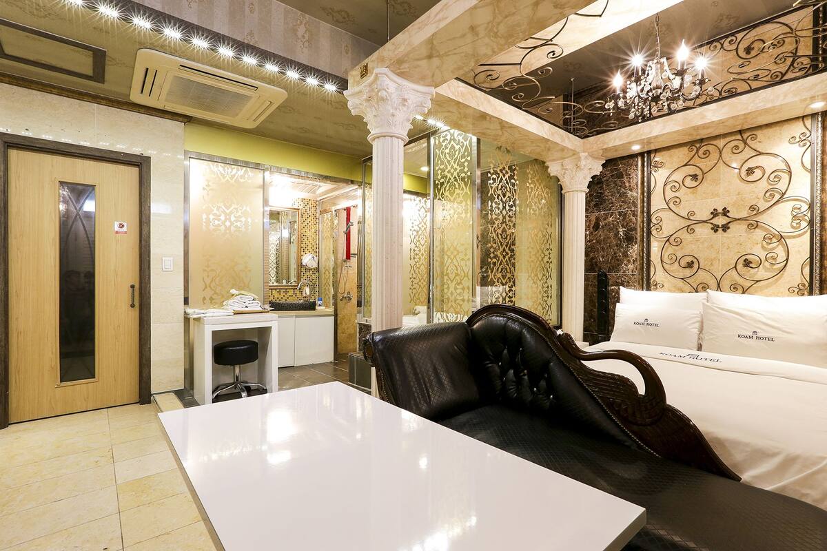 Quarto de hotel com uma grande mesa branca, um sofá de couro e uma cama com roupa de cama branca.