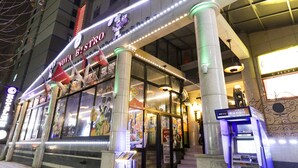 Ingresso di un hotel con insegna al neon, ampie colonne e un chiosco per pagamenti digitali.