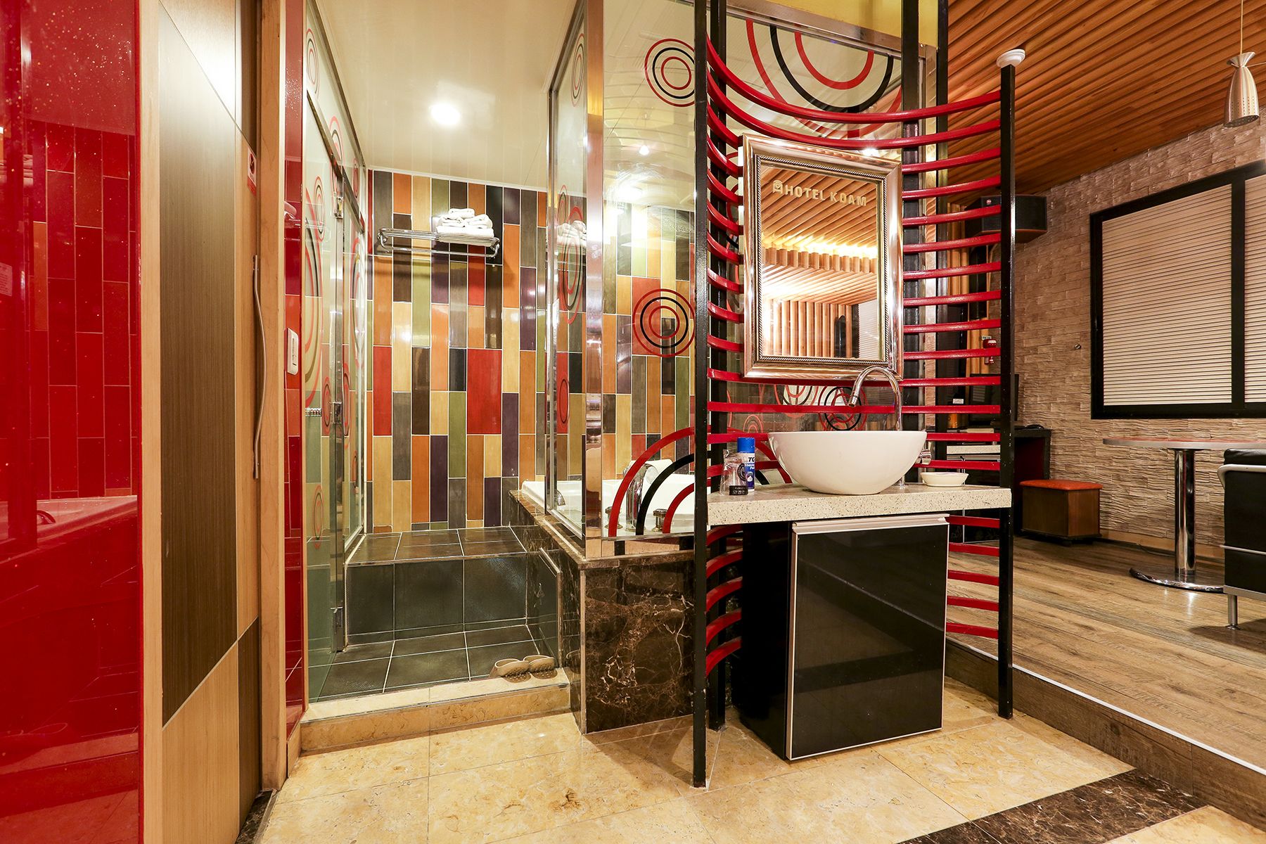 Ein modernes Badezimmer mit einer Duschkabine aus Glas, einem weißen Waschbecken mit großem Becken und einem Handtuchhalter in Rot und Schwarz.