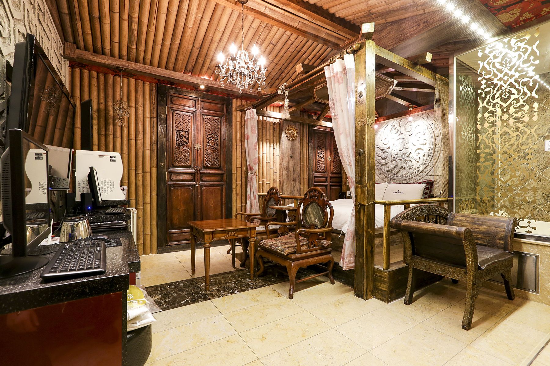 A traditional room with wooden furniture, a desk with a computer, and a bed with ornate headboard.