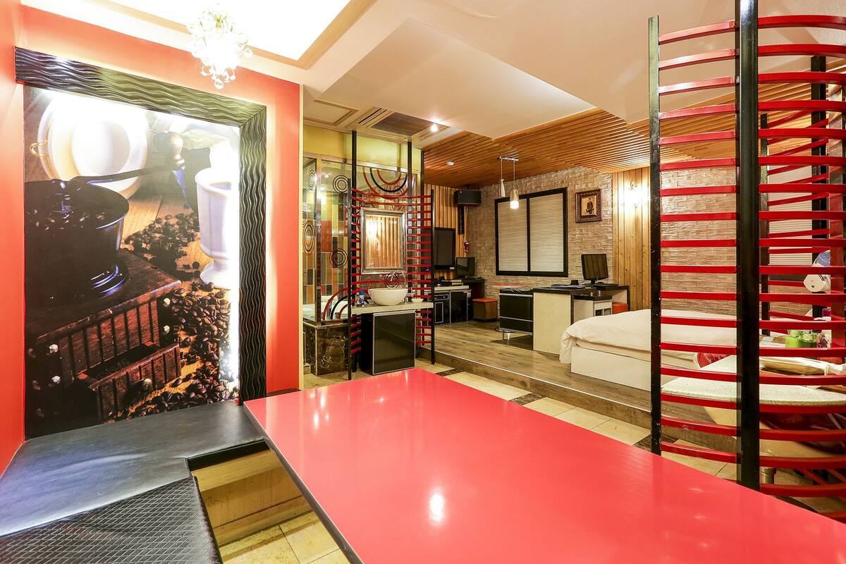 Quarto de hotel moderno com uma mesa vermelha, área de cozinha, banheiro e escada.